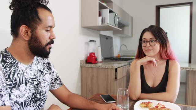 Joven pareja de mexicanos platicando y comiendo pizza en casa 