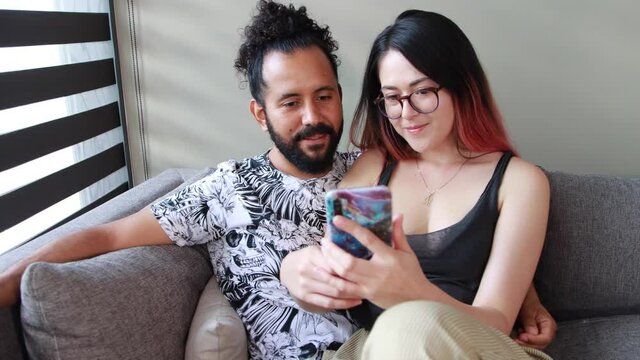 joven pareja mexicana pasan tiempo juntos en casa sala sofa escuchando musica y usando el telefono