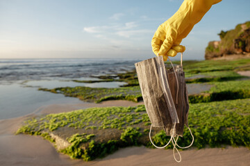 Closeup of a caucasian woman pick up used face mask. Garbage collector cleans the seashore....