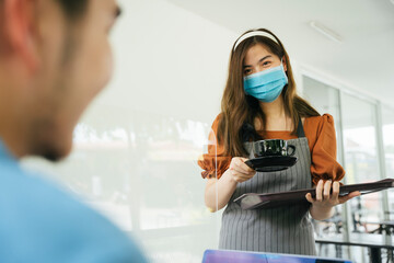 Waitress wear mask serving coffee cup to customer.