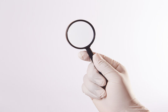 Mano de hombre con guante de l&aacute;tex sostiene una lupa. fondo blanco aislado
