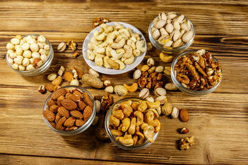 Assortment of nuts on wooden table. Almond, hazelnut, pistachio, peanut, walnut and cashew in small bowls. Healthy eating concept