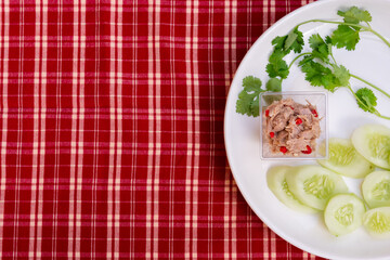Spicy salad with mini tuna and cilantro and cucumber slices on a white plate. Red cloth background, gingham.
