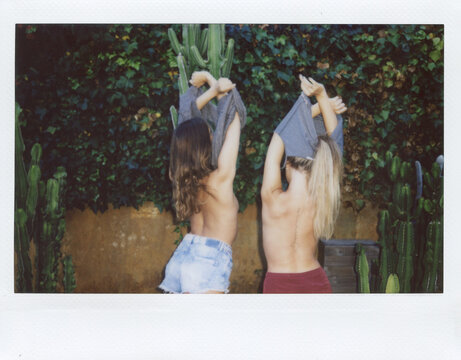Back view of girlfriends taking off t-shirts in garden
