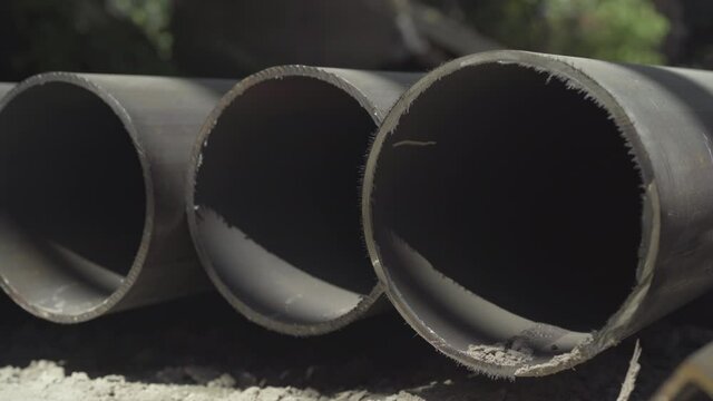 Close-up of huge metal pipes lying under sunlight outdoors. Industrial tubes on factory or plant or manufacturing site.