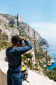 A young man / hiker ontop of a cliff taking photographs of coast / blue ocean