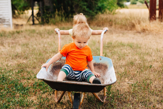Big sister gives her little brother a ride in a wheelbarrow.