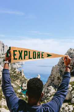 A man holding up an pennant that says Explore infront of cliff and ocean.