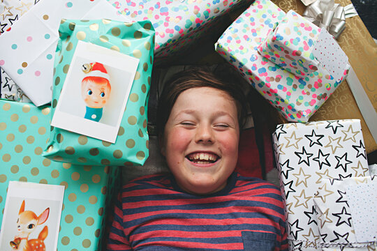 A young boy lying on floor surrounded by Christmas presents