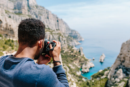 A young man / hiker ontop of a cliff taking photographs of coast / blue ocean
