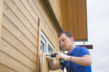 worker, blocks the window of the house with a protective shield made of wood, from thieves, when moving to another address