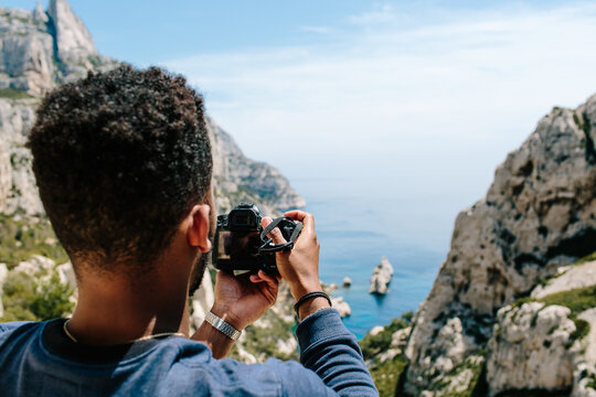 A young man / hiker ontop of a cliff taking photographs of coast / blue ocean