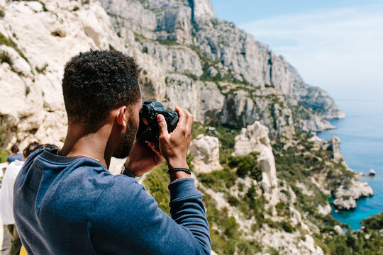 A young man / hiker ontop of a cliff taking photographs of coast / blue ocean