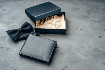 Black leather wallet and bow-tie on grey background