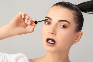 Fototapeta premium Beautiful young woman with fake eyelashes on lips and mascara against light background