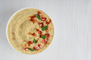 Top view of single savory organic homemade hummus thick spread made from mashed chickpeas used especially as a dip decorated with pomegranate seeds and parsley served in bowl. Image with copy space