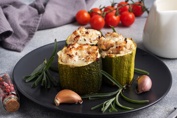 Baked stuffed zucchini columns with minced chicken and vegetables on a plate. Grey concrete background.
