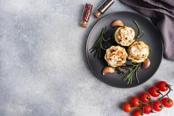 Baked stuffed zucchini columns with minced chicken and vegetables on a plate. Grey concrete background. copy space