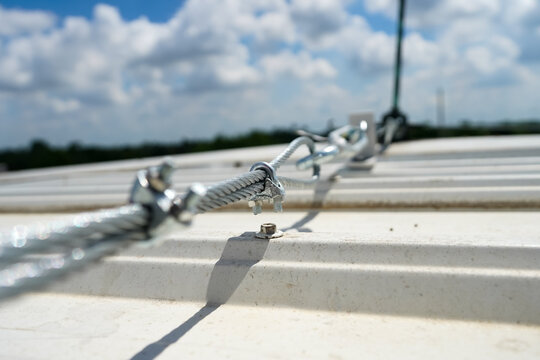 steel cable connect with lightning rod on rooftop above metal sheet in cloudy blue sky day stock photo
