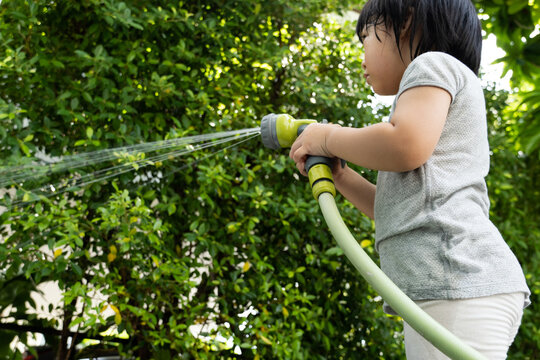 Funny moment of 3 Year old asian kid playing water with garden hose in backyard. Background concept  for play time and summer of children.