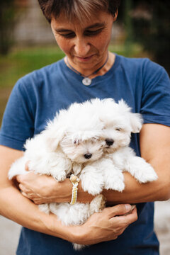 Woman looks with tender eye at two white puppies she holds in her arms