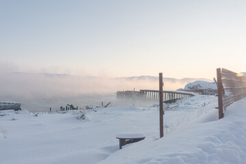 old wooden pier for large ships on the river bank covered in thick white fog from the water at dawn on a frosty winter day outside the Arctic Circle