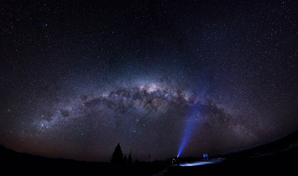 A male adventurer with strong headlamp under the full panorama of the Galaxy