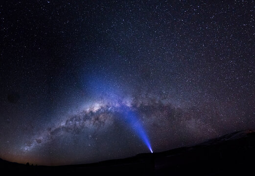 A male adventurer with strong headlamp under the full panorama of the Galaxy