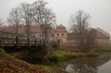 Fototapeta na wymiar The restored old Shlokenbek manor in Latvia. View from the river bank on an autumn foggy morning