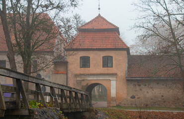Fototapeta na wymiar The restored old Shlokenbek manor in Latvia. View of the Arch from the river bank on a foggy autumn morning