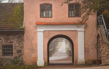 Fototapeta na wymiar Restored old Shlokenbek manor in Latvia. Arch passage road in fog