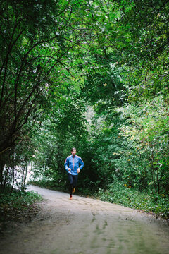 Man running in the rain on a gravel road surrounded by trees