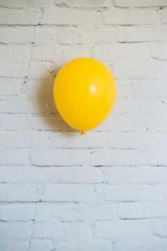 Yellow balloon floating in front of white bricks wall