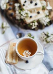 Sweet cake with fresh berries and spring flowers on wood plate,cup of tea, top view 