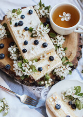 Sweet cake with fresh berries and spring flowers on wood plate,cup of tea, top view 