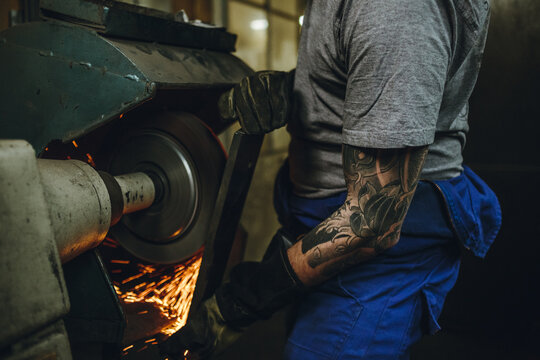 detail of tattoed metal worker grinding a metal plate