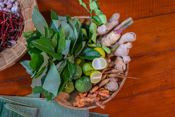 Thai herbs, betel leaves, bergamot, garlic, turmeric, lemon, ginger, galangal, dried chili, for food cooking a mixture of traditional ancient Thai alternative medicine in bamboo basket on wooden table