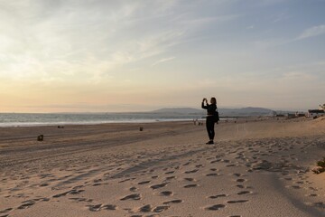 Beautiful caucasian woman walking along the beach at Costa da Caparica near Lisbon city center. Beautiful young woman with leather jacket relaxing on the beach at sunset in Caparica. Portugal, 2020