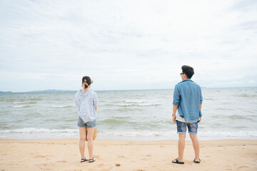 Asian couple traveler standing on the beach looking at the sea horizontal.