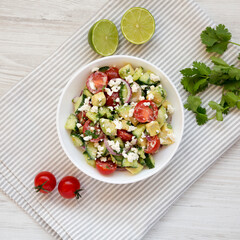 Delicious Avocado Tomato and Cucumber Salad in a bowl on a white wooden background, top view. Flat lay, overhead, from above.