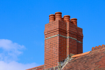 Old brick chimney pots on a victorian building roof against a blue sky background
