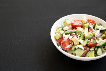 Delicious Avocado Tomato and Cucumber Salad in a white bowl on a black surface, side view. Copy space.