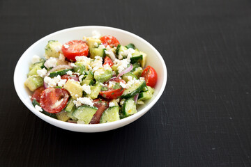 Delicious Avocado Tomato and Cucumber Salad in a white bowl on a black background, side view. Space for text.