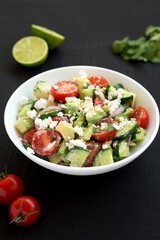 Delicious Avocado Tomato and Cucumber Salad in a white bowl on a black background, low angle view. Close-up.