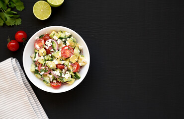 Delicious Avocado Tomato and Cucumber Salad in a white bowl on a black background, top view. Flat lay, overhead. Copy space.