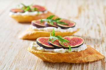 three bruschetta with ricotta and fresh figs on a white wooden table, horizontal composition.