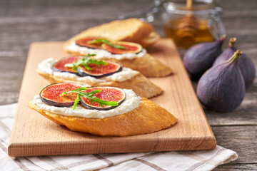 Bruschetta with ricotta cheese, ripe figs and honey served on a small cutting board.