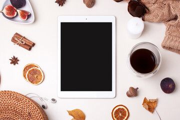 Blank white tablet, autumn leaves, figs, a warm sweater and a glass of coffee on a white background. View from above