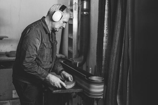 senior woodworker grinding a piece of wood on a belt sander in black and white