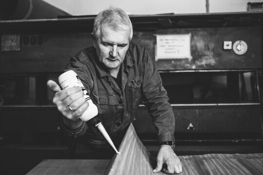 portrait of a senior carpenter applying glue on wooden veneer in black and white